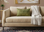 Beige sofa with a green pillow and white blanket in a living room setting.